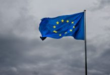 Ukraine’s Zelenskyy Addresses EU Leaders on Support & US Policy A lively EU flag dances in the wind with a striking cloudy sky.
